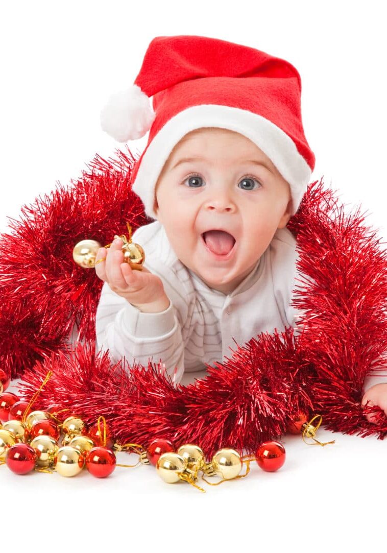 Little boy wearing a Santa hat and playing with baubles. Isolated on white background