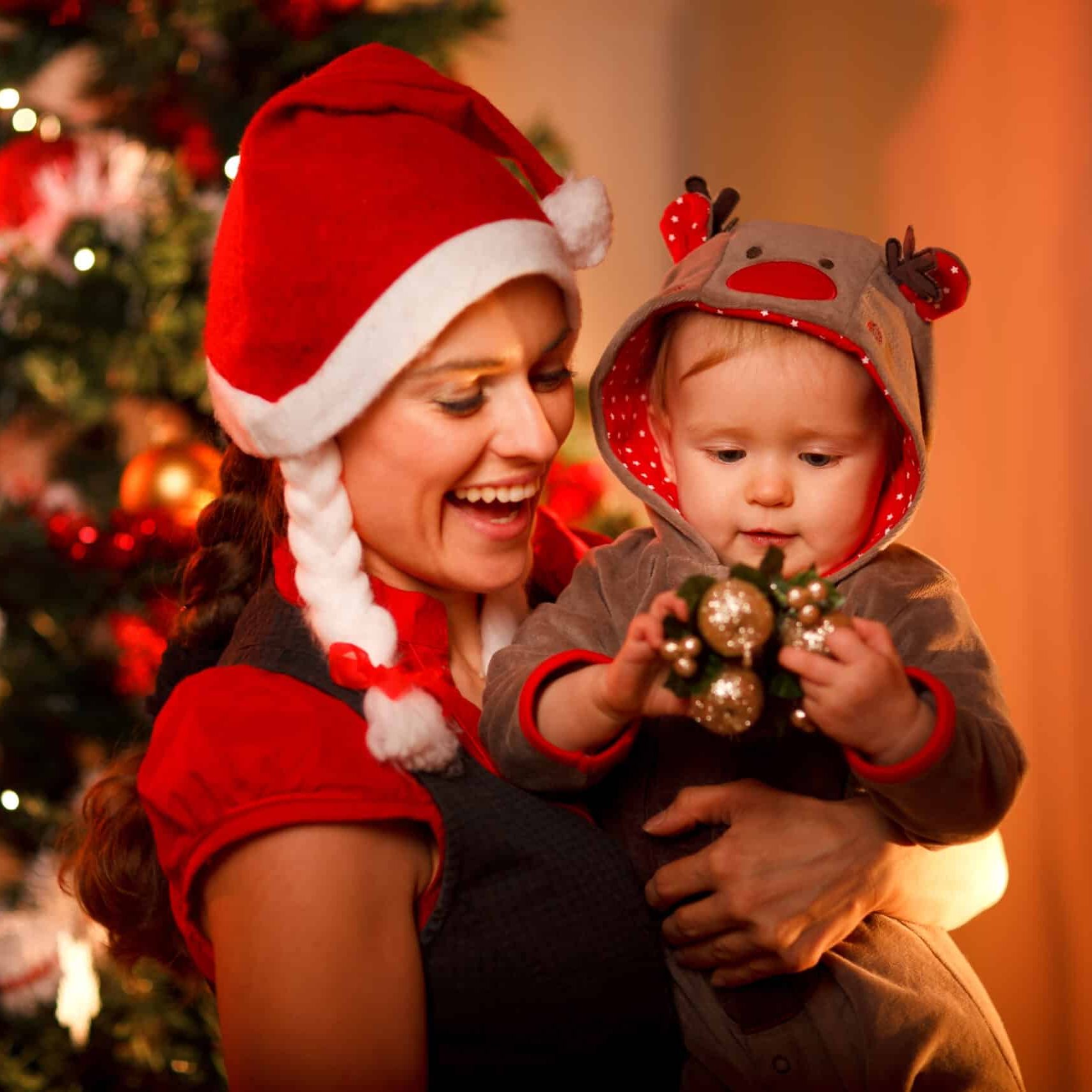 Smiling mother playing with lovely baby near Christmas tree